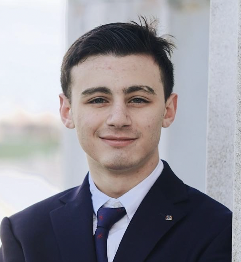 Man with brown hair smiling in suit and tie